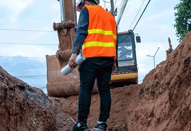 travailleur dans un troue sur un chantier équipé d'EPI et d'un carnet à la main