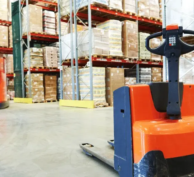 dépôt avec des rangements et pleins de marchandises et au premier un gerbeurs et garé devant