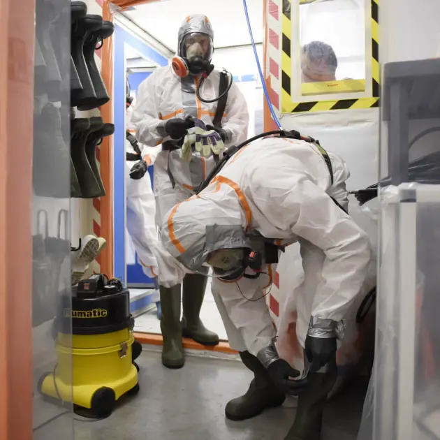 plusieurs personnes dans un salle équipé de combinaisons pour traiter l'amiante